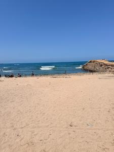 a sandy beach with people in the ocean at APPARTEMENT DE LUXE 3 Façades in Ben Slimane
