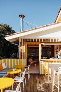 a patio with yellow tables and chairs on a deck at Hotel des Dunes in Cap-Ferret