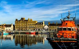 an orange boat is docked in a harbor with buildings at Havrock in Orkney