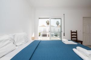 a white bedroom with a blue bed with a large window at Montesol by ALGARVEMANTA in Manta Rota