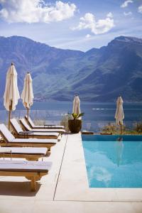 a pool with white umbrellas and lounge chairs at Hotel Mercedes in Limone sul Garda