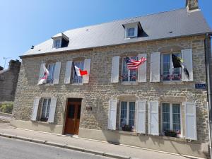 an old stone building with flags on the windows at Chambres d'Hôtes et Table d'Hôtes- Valentine 44 in Sainte-Mère-Église