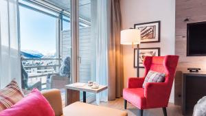 a living room with a red chair and a large window at AMERON Davos Swiss Mountain Resort in Davos
