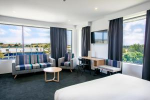 a hotel room with a bed and chairs and a desk at Alpha Hotel Eastern Creek in Blacktown