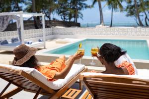 two women sitting in chairs drinking wine by a swimming pool at ZAN Orient Bwejuu Hotel in Makunduchi