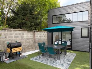 a patio with a table with a blue umbrella and a grill at Le rivage 44 in Bénouville