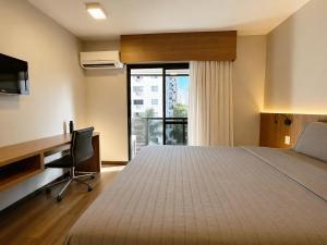 a bedroom with a bed and a desk and a window at Flat Executive City Jardins in São Paulo