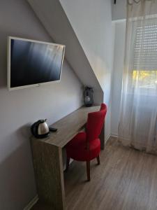 a desk with a red chair and a television on the wall at Relais du méne in Collinée
