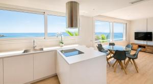 a kitchen with white cabinets and a dining room with a table at Vista Roses Mar - Ancla Mar in Roses