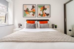 a white bedroom with a large white bed with paintings on the wall at Luxury Apartment Close to Elstree & Borehamwood Station in Borehamwood