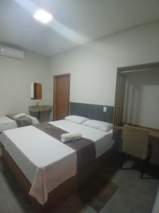 a hotel room with two beds and a chair at Slan Ville Hotel in Chapadão do Sul