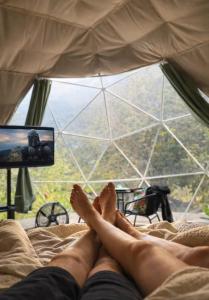 a person laying on a bed watching a television at Cerro Verde Glamping Cartago in Lourdes