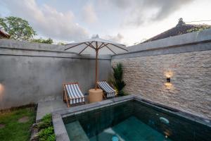a swimming pool with two chairs and an umbrella at Maheeka Villa, Sanur in Sanur