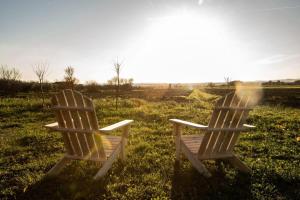 two wooden chairs sitting in a field with the sun in the background at Dolce Casa 2 by Tiny Away in Rigutino