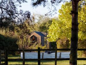 a small house behind a fence with a tree at Vilasini Hut by Tiny Away in Great Horkesley