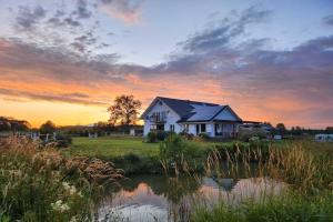 a house in a field next to a pond at Agritourism by the sea in Ładzin