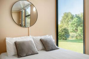 a mirror above a bed in a bedroom with a window at Hinterland Hideout by Tiny Away in Myocum