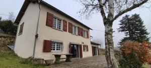 a white house with red shuttered windows and a tree at Balcon des fées in Le Malzieu-Ville