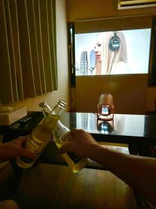 a person holding two bottles of beer in front of a tv at 古民家松 in Isumi