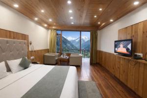 a bedroom with a bed and a television and mountains at Hotel The Himalayan Riverside - Most Awarded Property of Manali 2025-26 in Manāli