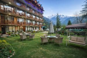 a hotel yard with tables and chairs and mountains at Hotel The Himalayan Riverside - Most Awarded Property of Manali 2025-26 in Manāli