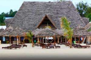 a building with chairs and straw umbrellas on a beach at 27Azmaa hotel & safaris in Zanzibar City