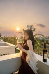 a woman sitting on a balcony holding a glass of wine at The Happy Marina Hotel Phú Quốc - Sunset & Ocean View in Phú Quốc
