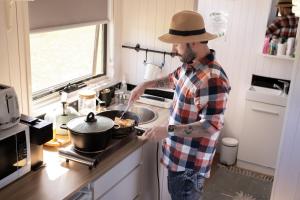 a man in a hat cooking in a pan in a kitchen at Odyssean Tiny House B by Tiny Away in Cessnock