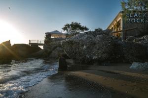 a rocky beach with a building and the ocean at Black Rocks Family Beach Resort in Agios Gordios +40 photos