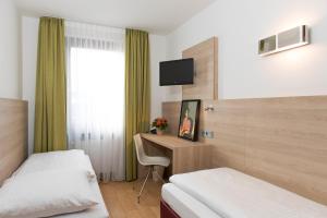 a hotel room with two beds and a desk with a television at Hotel Amba in Munich