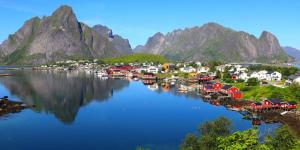 a village on the water with mountains in the background at Lofoten Cruise & Hotel in Svolvær