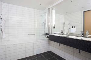 a white tiled bathroom with a tub and a sink at Scandic Meyergården in Mo i Rana