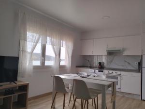 a kitchen with white cabinets and a table and chairs at Casa Camiño dos Faros in Sinde