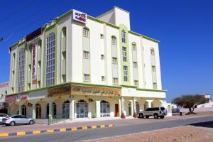 un edificio amarillo y blanco con coches estacionados frente a él en Super OYO 107 Al Areen Hotel Apartments, en Shāhiq