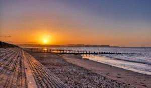 a sunset over a beach with a pier at 2 Bedroom - Seaside Apartment in Dawlish Warren