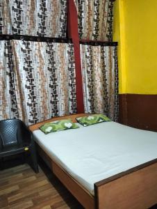 a bedroom with a bed and a chair in front of a curtain at Oasis Lodge in Jorhat