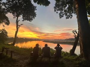three people sitting on a bench watching the sunset at YHA Backpacker Hostel Sauraha in Sauraha