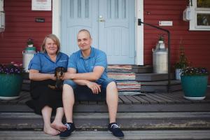 a man and woman sitting on the steps of a house with a dog at Villa Korkatti in Haapavesi