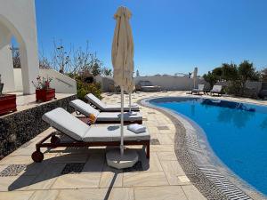a pool with two lounge chairs and an umbrella at Villa Thea in Kamari +47 photos