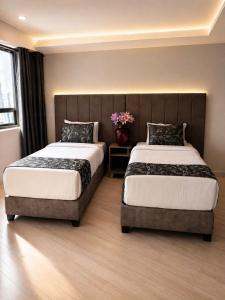 a bedroom with two beds and a vase with flowers at Aw Hotel Embassy Corner - Corferias, Embajada EEUU & Vive Claro in Bogotá
