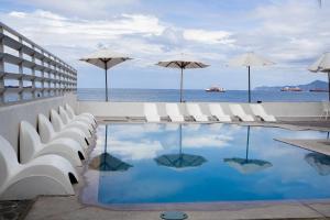 a pool with white chairs and umbrellas and the ocean at Best Western Plus Luna del Mar in Manzanillo