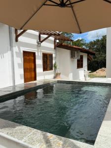 a swimming pool in front of a house with an umbrella at Casa Sol Piscina e Cachoeira in Pirenópolis