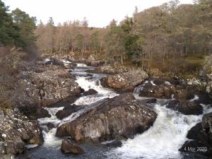 a river with rapids on rocks and trees at Achness Hotel in Lairg
