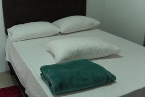 a white bed with white pillows and a green pillow at Kitnet confortável in Foz do Iguaçu