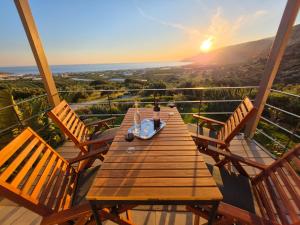 a woman sitting on a wooden table on a deck with the sunset at Casa di Olive Luxury Secluded Sea View Villa in South Crete in Goúdhouros