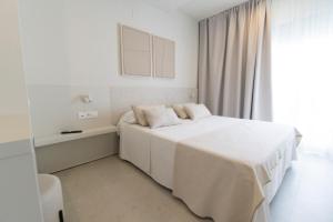 a white bedroom with a bed and a window at Hotel Roca Plana in L'Ampolla