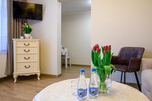 a table with a vase of red flowers and two bottles at Apartamenty 40 in Ciechocinek