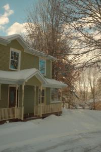 a yellow house with a porch in the snow at Maison Hôte in Magog-Orford
