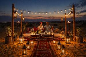 a couple sitting on a bed in the desert with lights at Sky Desert Safari With Swimming Pool in Jaisalmer