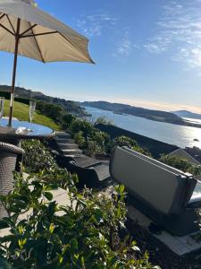 a bench with an umbrella and a table and water at Tigh Beag Pod with Hot Tub in Oban